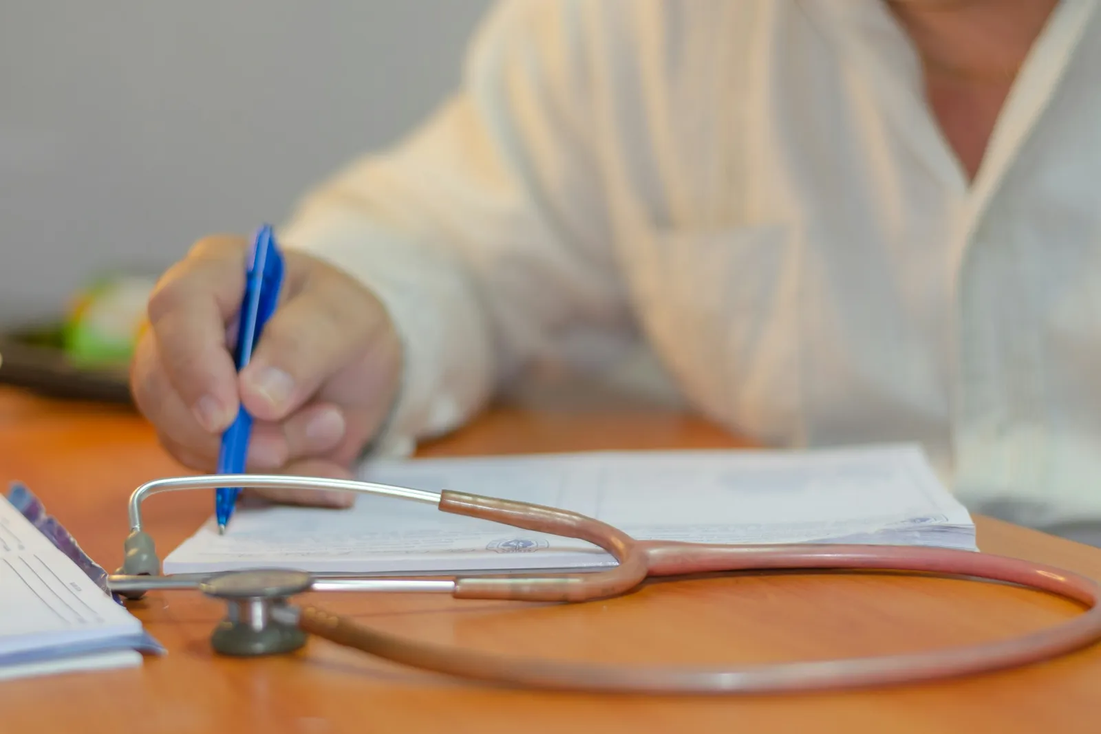 A doctor's hand writing on a prescription pad beside a stethoscope