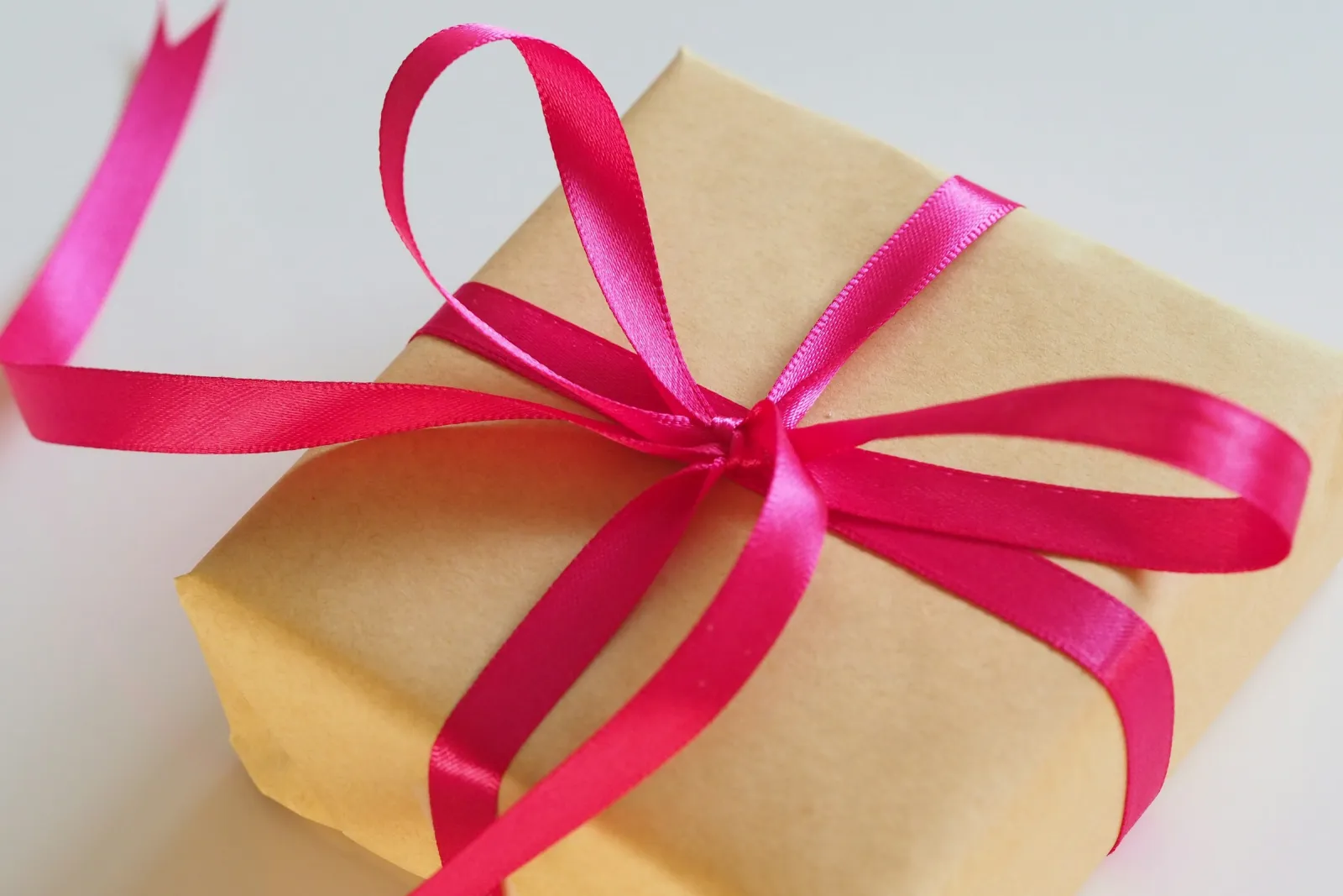 An elegant gift box wrapped in kraft paper with a pink ribbon bow
