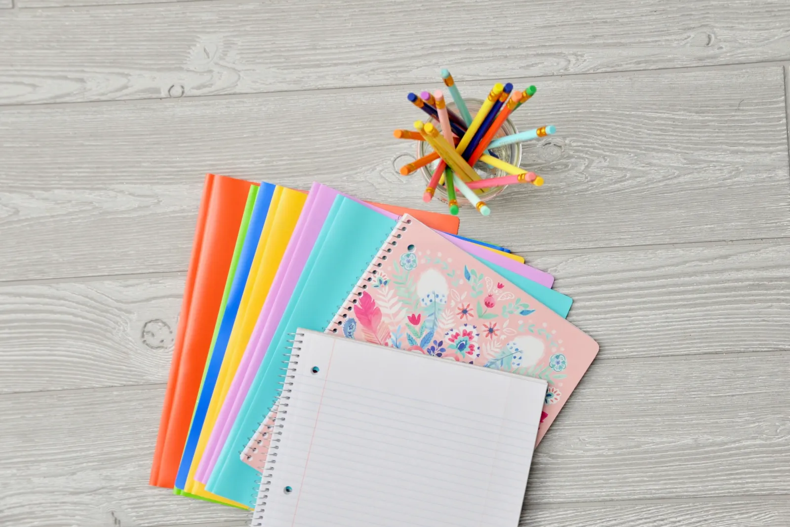 Colourful notebooks and pencils laid out on a wooden desk